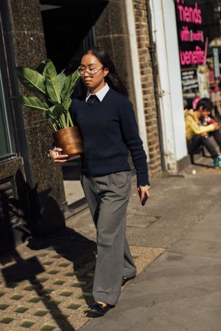 woman wearing a white button-down shirt, navy sweater, and gray trousers