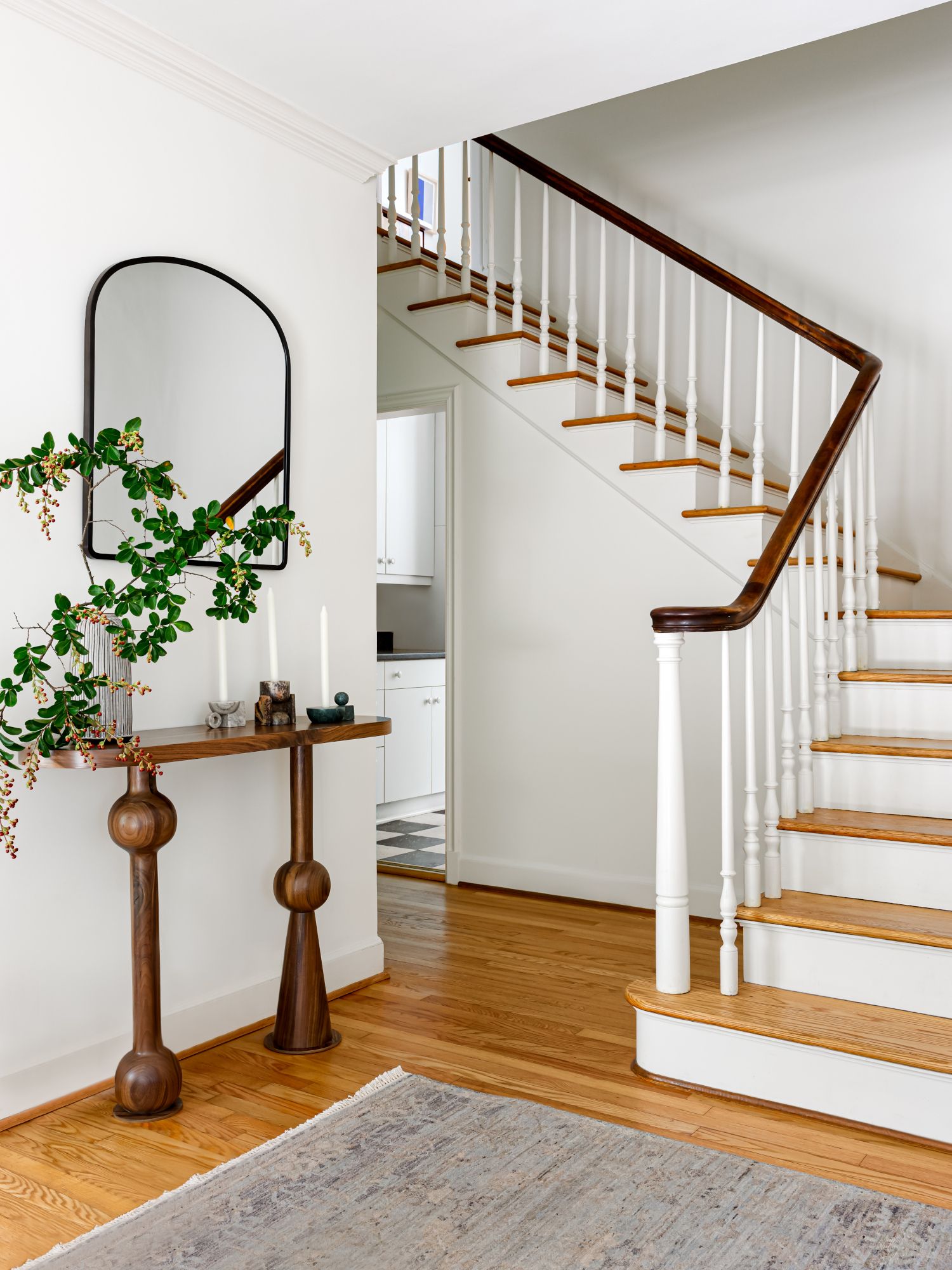 White hallway with corner staircase and sculptural console table in dark wood