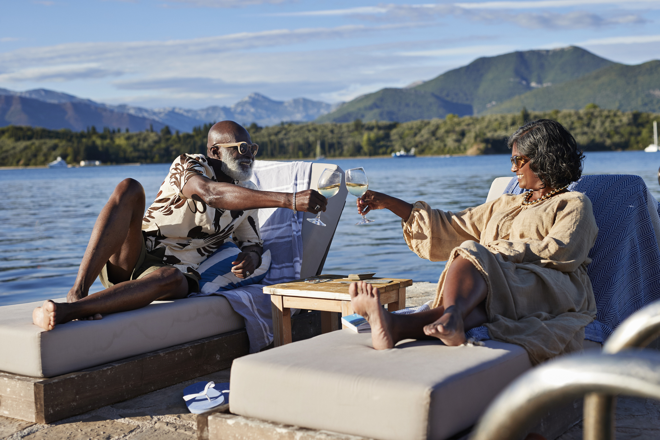 A senior couple clinks glasses while relaxing by a lake.