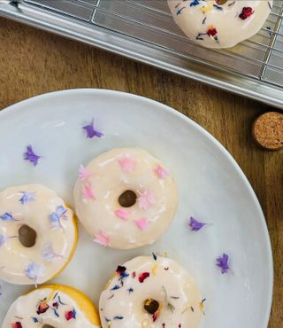 A white plate with donuts covered in flower sprinkles sitting on a wooden table