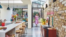 an open plan modern kitchen idea in an extension of Victorian terrace house with island, metal frame windows and exposed brick