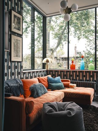 A living room with an orange sofa filled with cushions and a throw