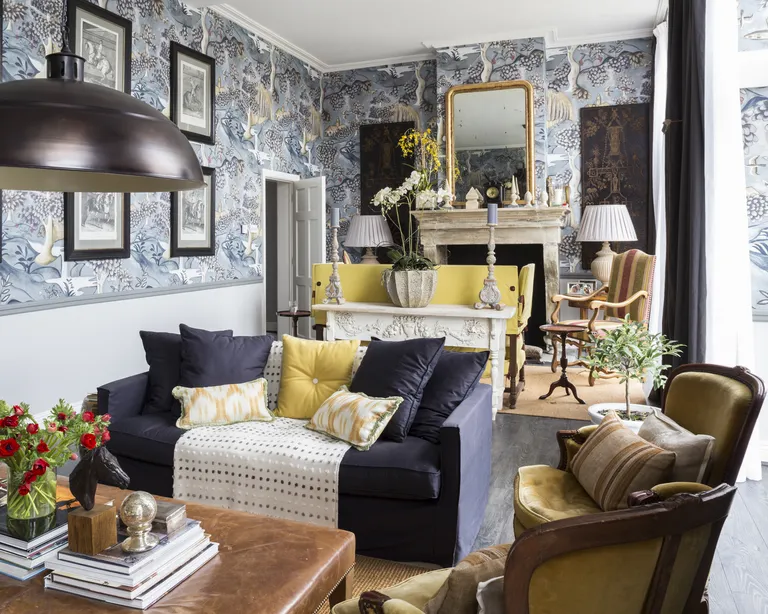 A traditional living room with pale blue wallpapered walls, and a navy blue sofa with yellow soft furnishings