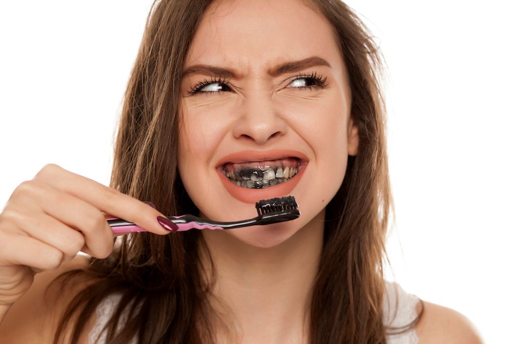 A woman brushing her teeth with activated charcoal toothpaste.