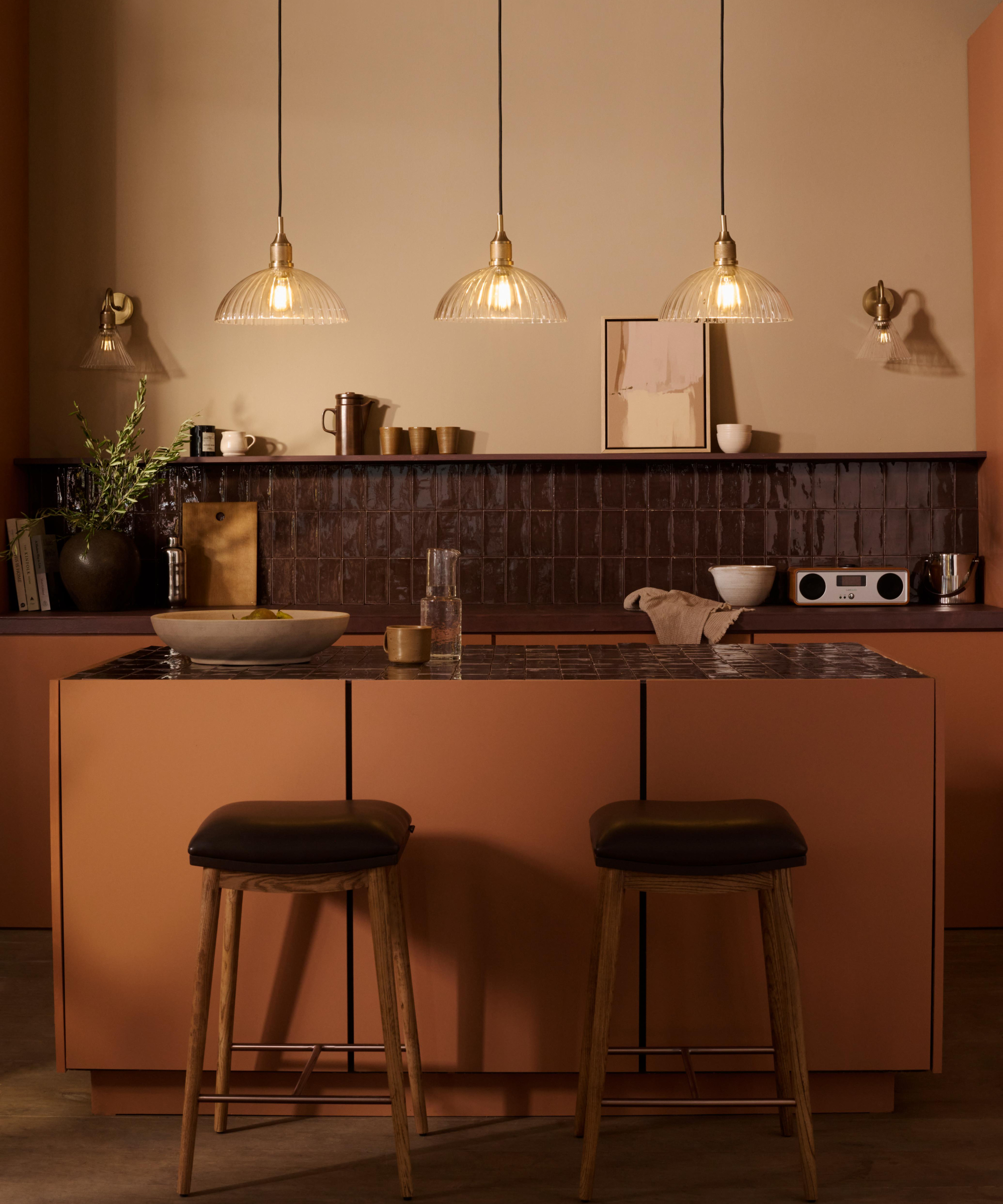 3 glass pendant lights hanging above kitchen island with dark worktop and two bar stools to one side