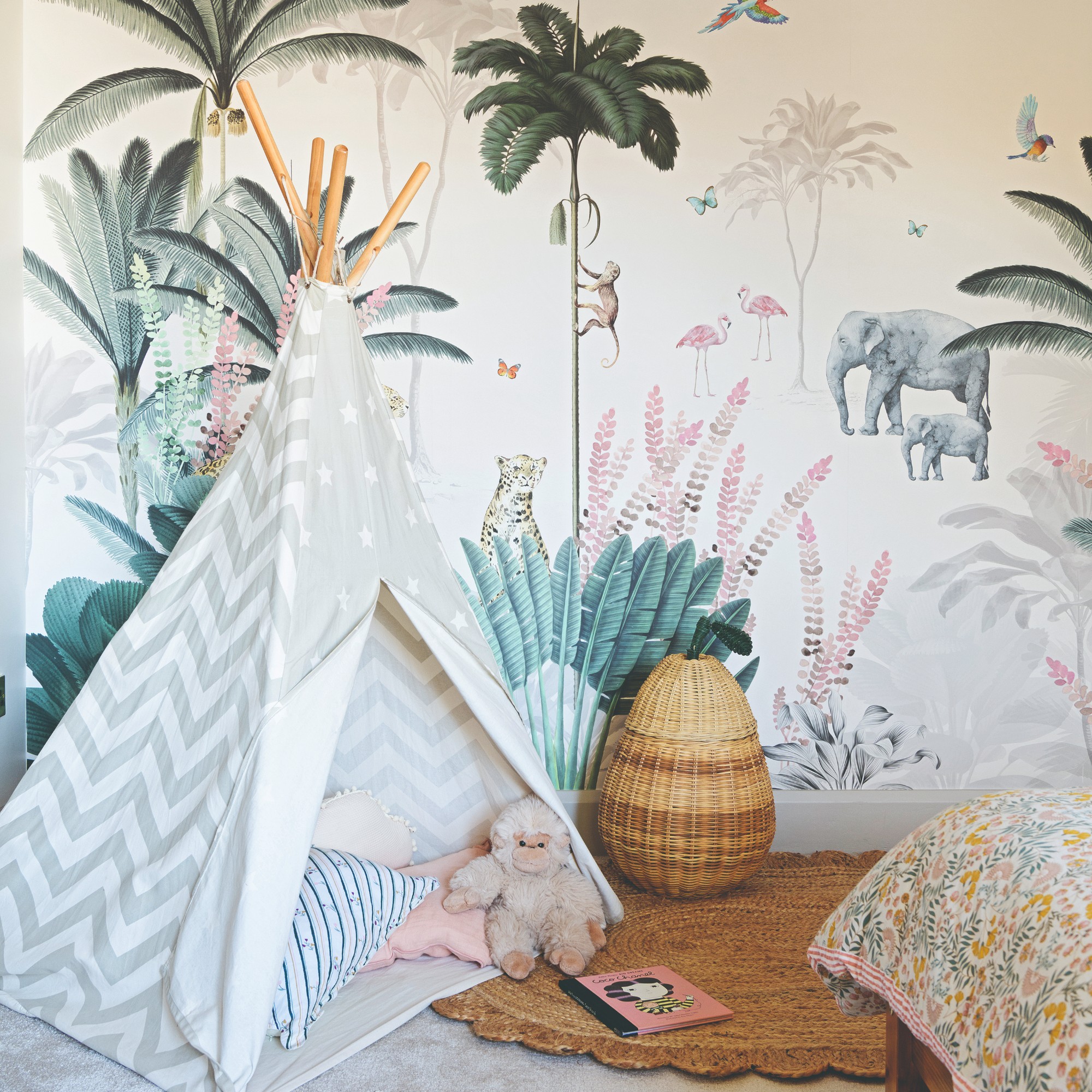 A children's bedroom with a tropical wallpaper, a teepee tent and a pear-shaped storage basket
