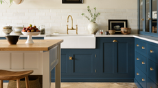 White kitchen with dark blue deVOL cabinets, wooden floors and wooden island with white sides and basket storage underneath