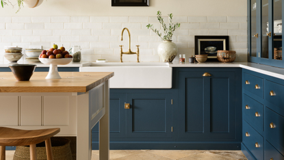 White kitchen with dark blue deVOL cabinets, wooden floors and wooden island with white sides and basket storage underneath