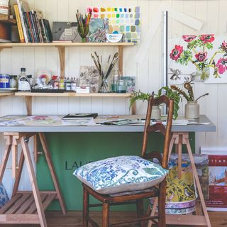 A craft room with a large desk and two floating shelves above storing tools and supplies