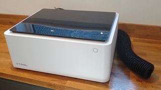 xTool M1 review; a white laser cutter, a large box, on a wooden table