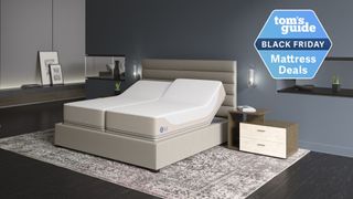 Sleep Number iLE Limited Edition 360 smart bed in room with grey tapestry rug, dark grey walls, wooden bedside table and wall-mounted lamps. 