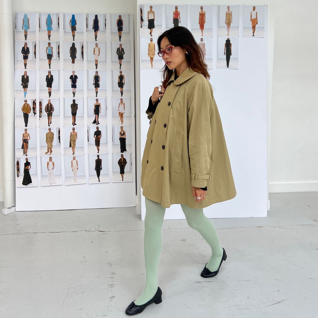 Vivian Li wearing blue tights and a brown jacket in front of a runway images of the Courrèges Spring 2026 show