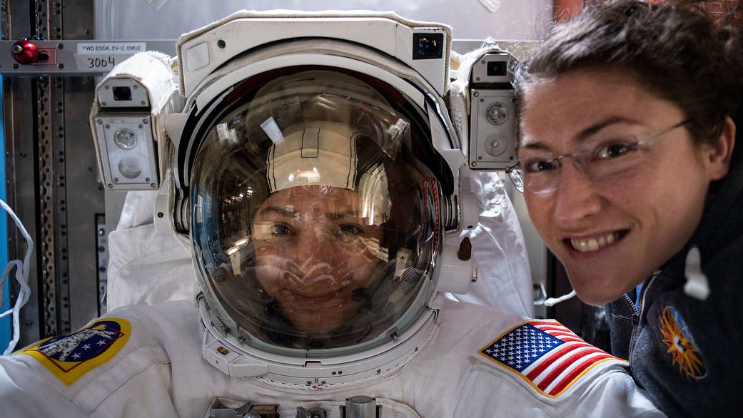 woman in spacesuit next to woman in astronaut flight suit floating in space station