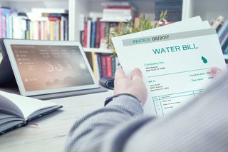 Man holds water invoice with laptop in the background