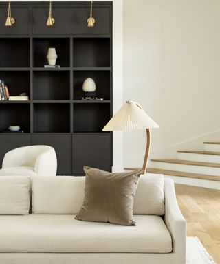 neutral quiet luxury living room with dark wood bookshelf and pleated floor lamp