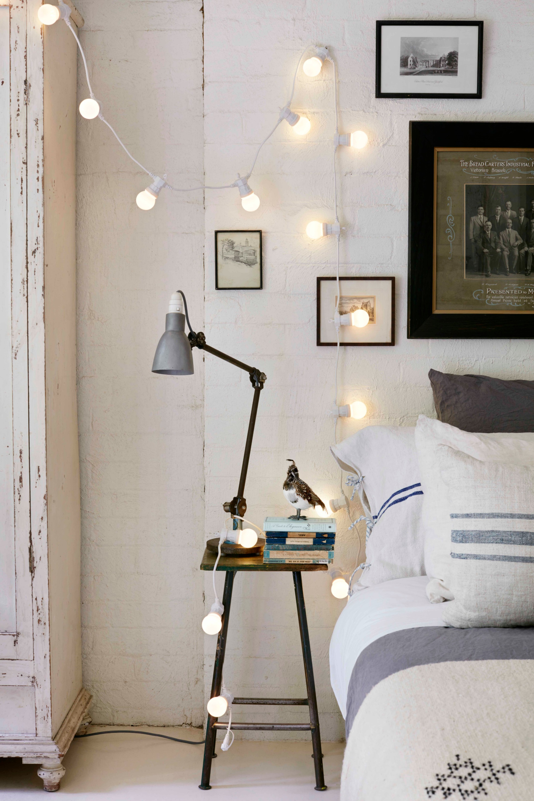 White bedroom with exposed brick wall and fairy lights