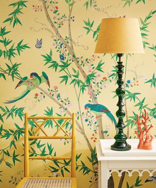 Yellow hallway with tropical, jungle-inspired yellow wallpaper with birds and leaves, white wooden console table with table lamp with yellow shade, painted yellow chair