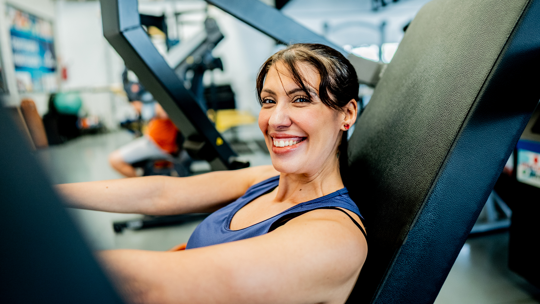Woman sitting on a weights machine at the gym smiles at the viewer