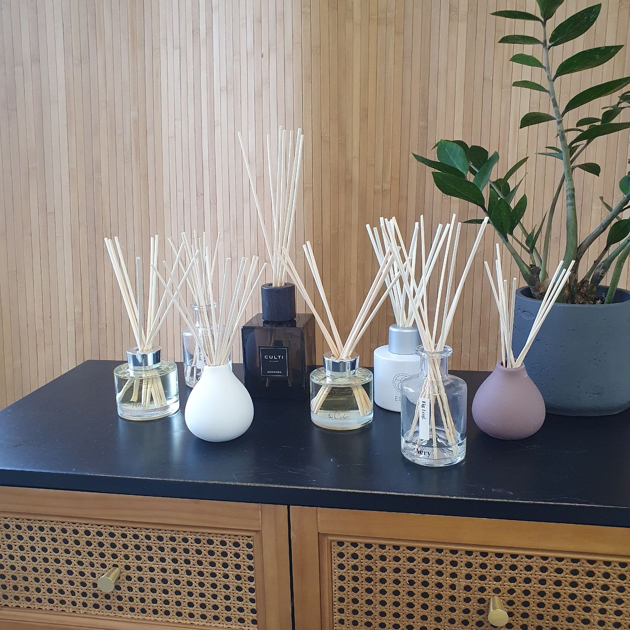 A group of reed diffusers on a cabinet next to a plant