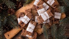 Christmas flapjacks wrapped in white paper and brown string on a wooden board surrounded by pinecones