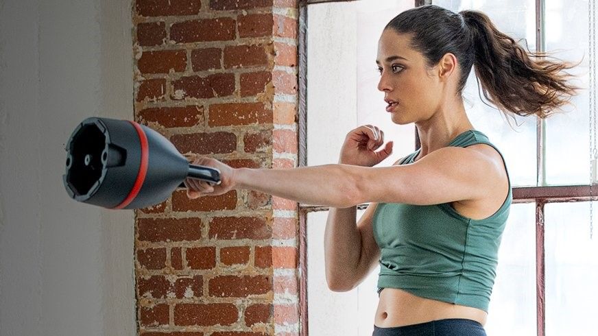 Fit young women performing one-handed kettlebell swings in a room with brick walls