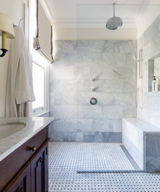 Wet room with marble shower bench and floor tiles, glass shower door, blind and basin unit , tiled floor