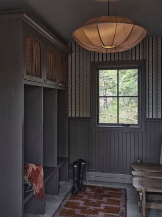 Dark gray mudroom with built-in storage. There is a large fabric light fixture and half of the back wall has striped wallpaper