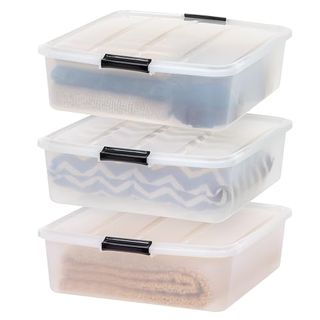 A set of three clear plastic rectangular storage bag with black slip handles and a lids. All on top of one another. FOlded blankets inside. 