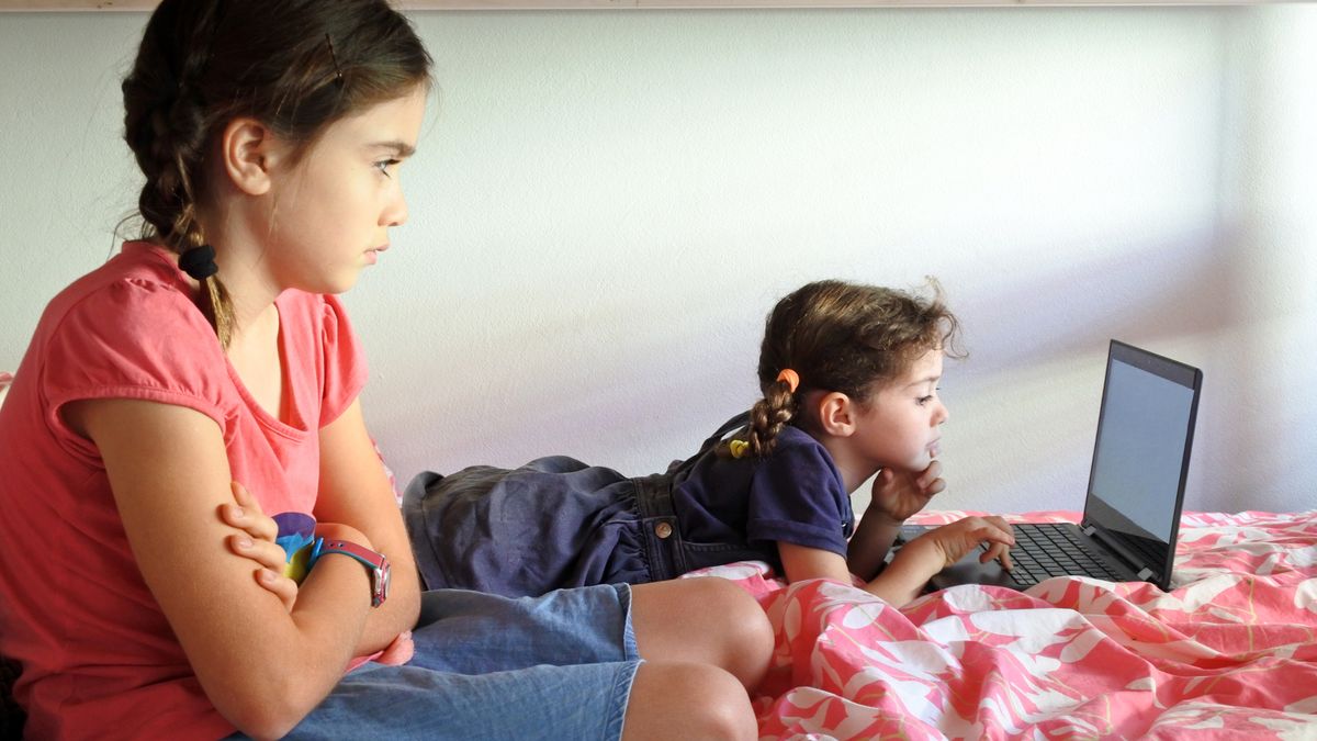 One young girl using laptop while second girl looks on