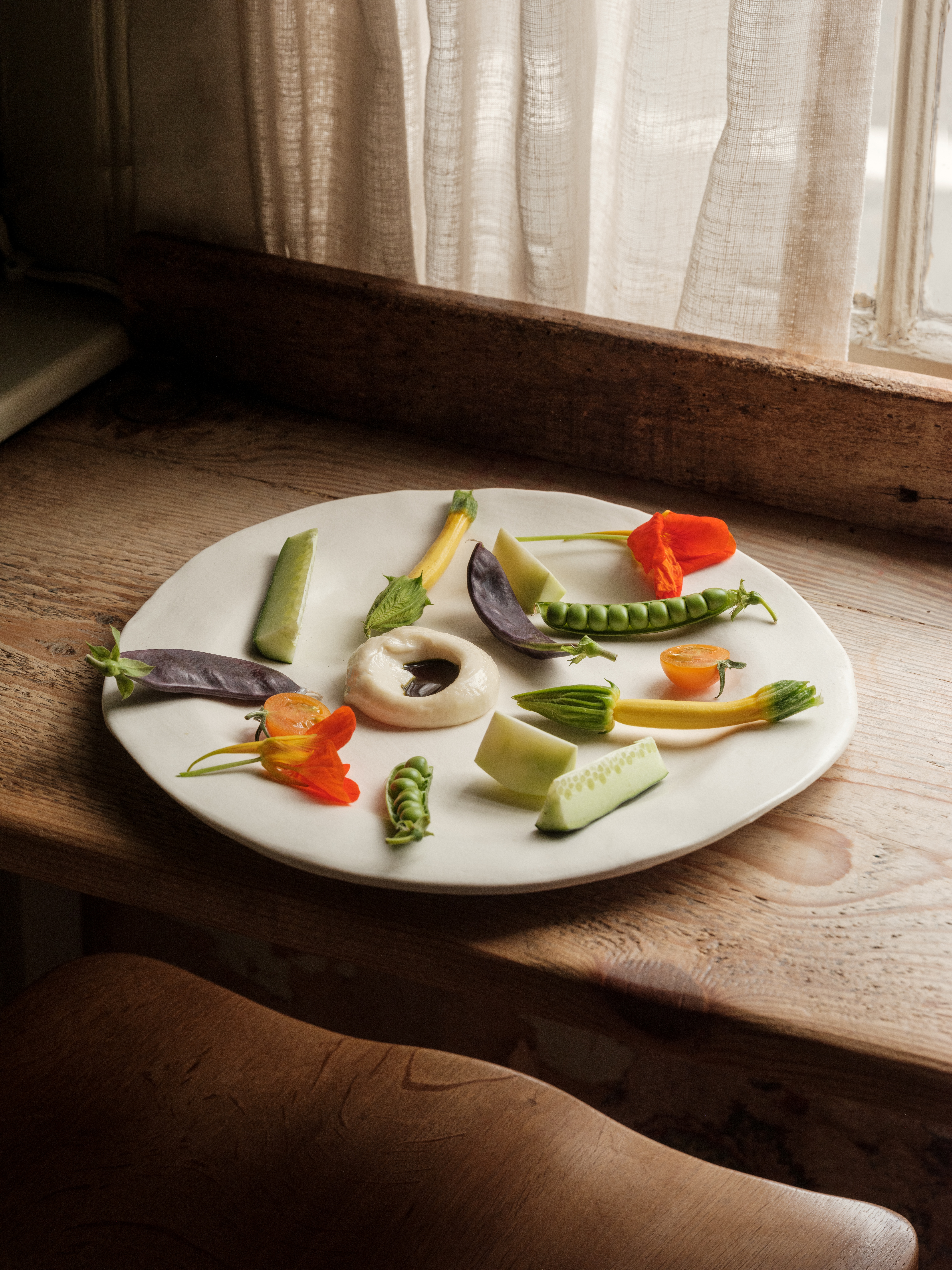 A series of shots depicting the interiors of a modernly renovated, old farmhouse in the countryside, mixing a rustic frame with plush textiles, textural surfaces, glass, wood, and chrome accents, and colorfully plated dishes.