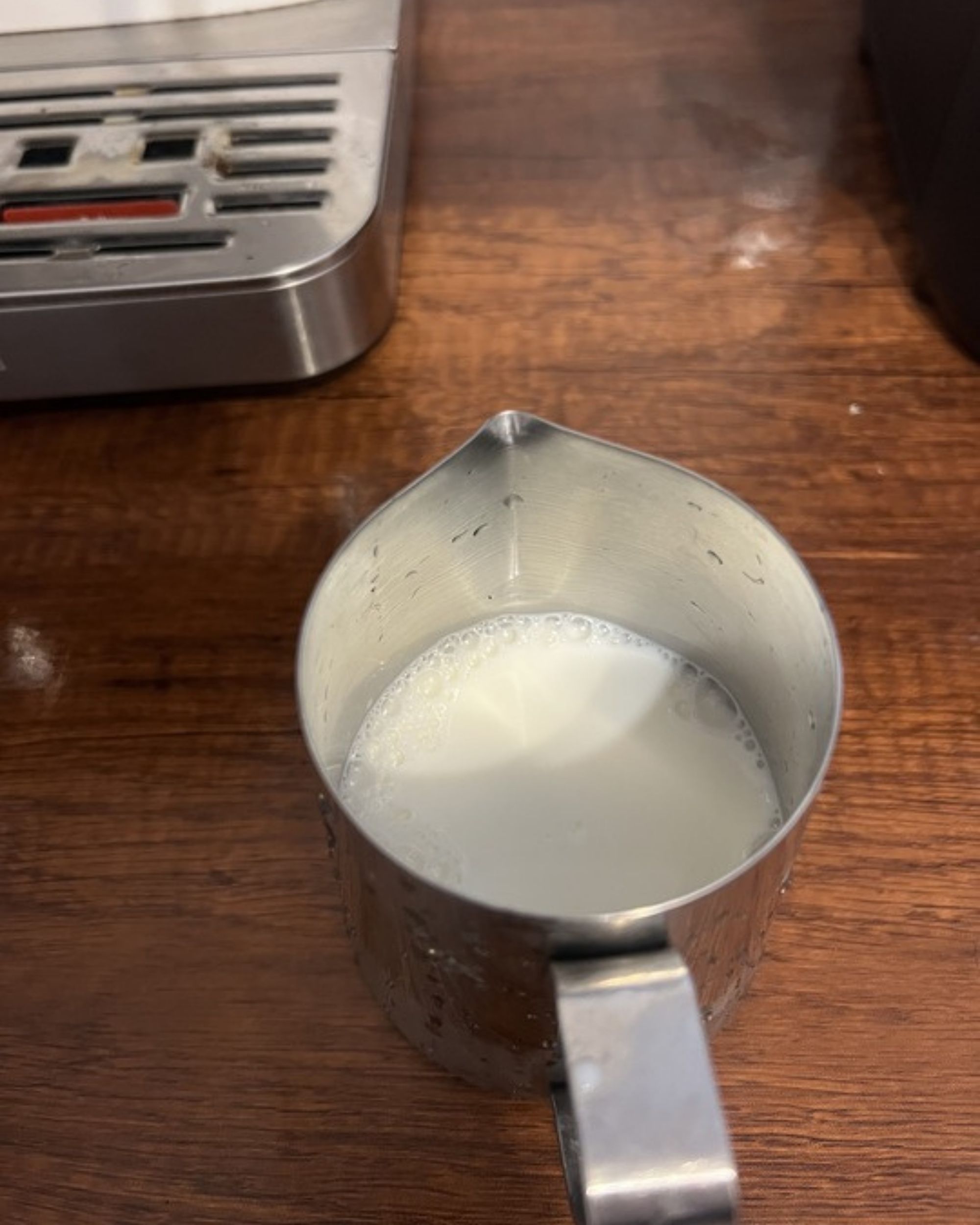 Image of a silver milk jug filled with milk on a wooden countertop