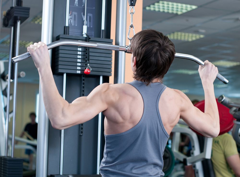 A teenage boy lifts weights in a weight room.