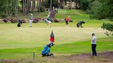A golfer in the foreground waiting for another golfer behind him on the fairway to hit his shot, with two other golfers also watching