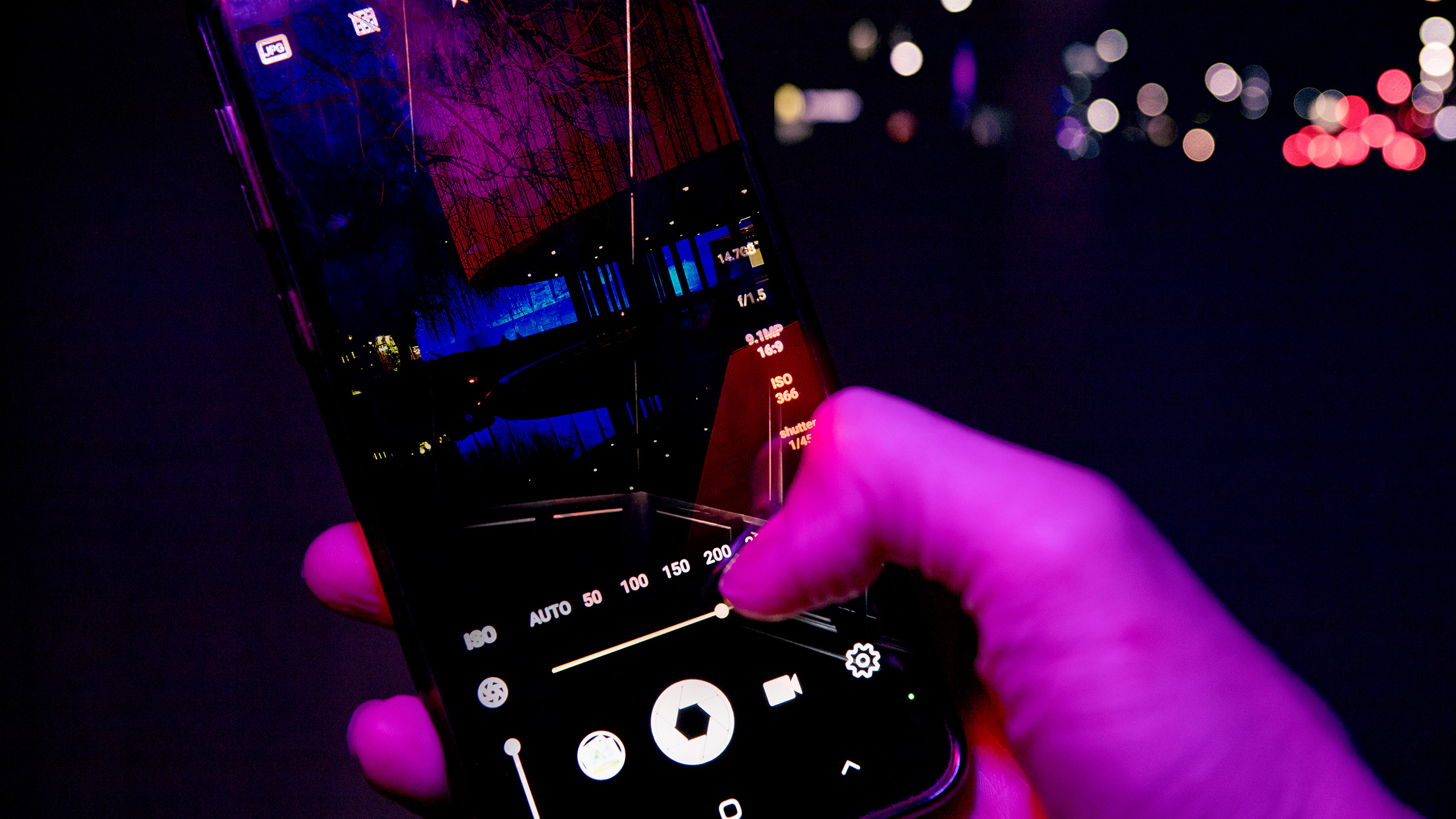 A hand adjusting the camera settings on a smartphone's illuminated screen, showcasing vibrant colors and night scenery