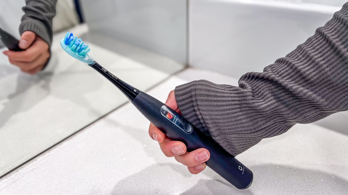 A hand holding the Oclean X Ultra S overa. bathroom countertop