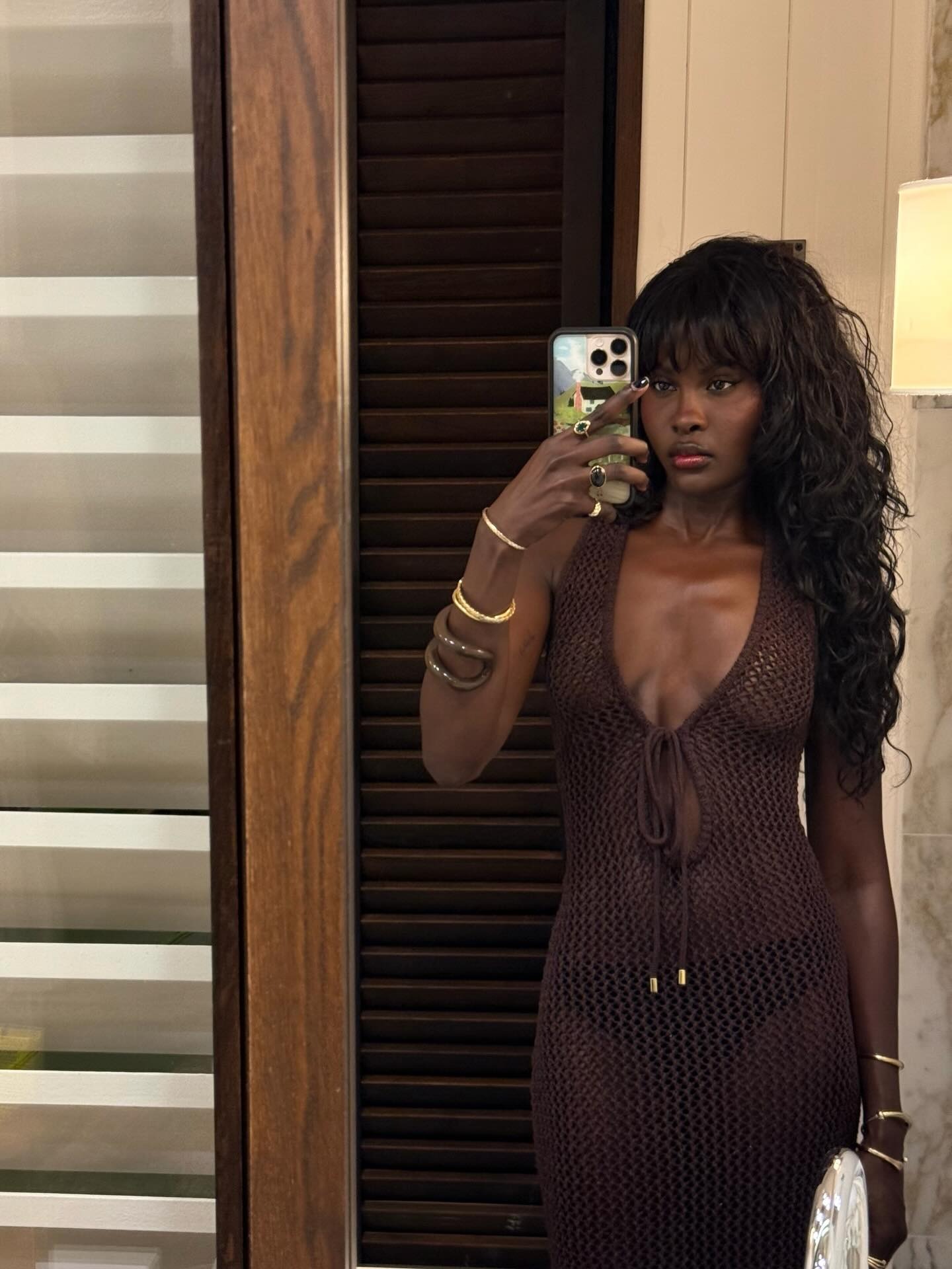 A woman taking a mirror selfie in a brown dress with a wavy, shag haircut and fringe