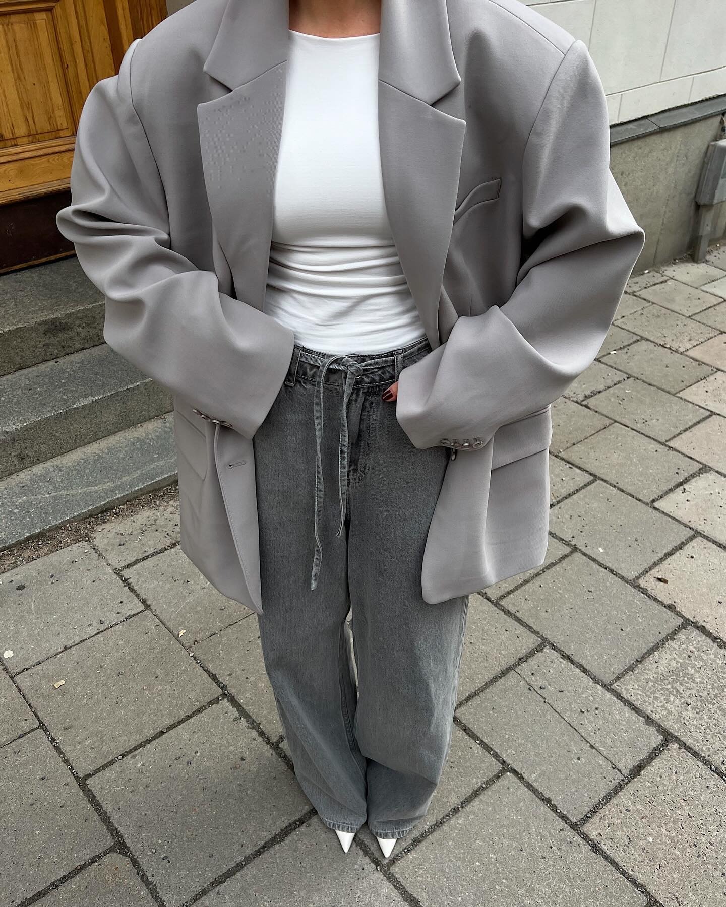 Fashion person Haaanna Johansson wears the drawstring jeans trend. She wears a grey blazer, white t-shirt grey drawstring jeans and white heel. she is stood looking at the pavement with here full look in sight. This image was recently taken from her Instagram.