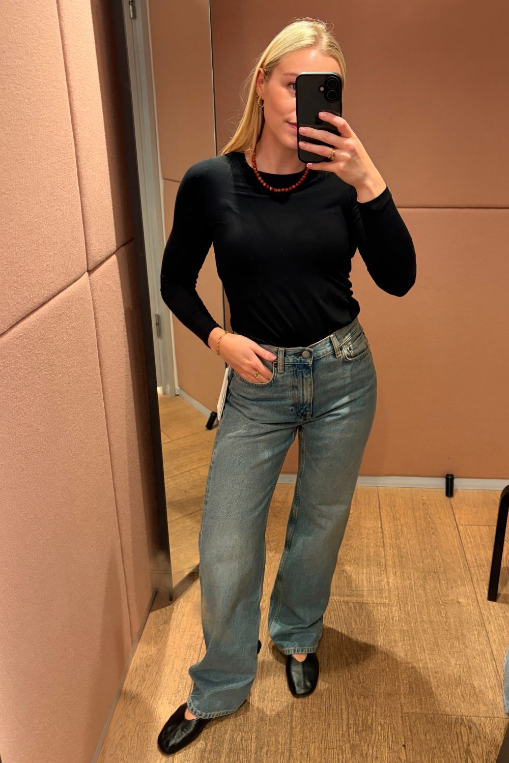 Shopping editor, Florrie, wears a black long sleeved top, COS Chord Straight Leg Jeans, black ballet flats and red bead necklace