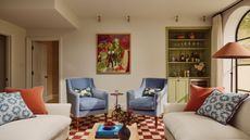 neutral living with a green painted home bar in the corner, beige sofas with red and blue cushions, a red checkerboard rug, and blue arm chairs