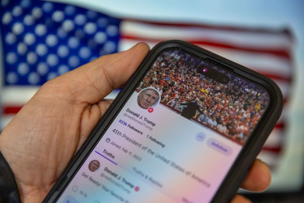 closeup of Donald Trump&#039;s profile on Truth Social app with an American flag in the background