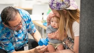 A woman holds her baby as they receive an MMR vaccine