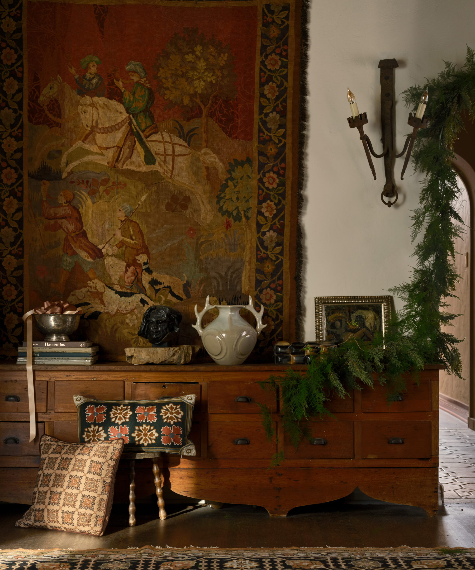 an antique credenza with decorative objects, pillows, artwork, and a large tapestry hanging behind