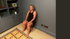 Kat doing wall sit exercise in living room at home