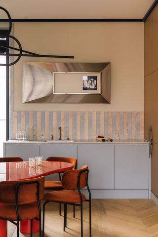 a light blue kitchen with red table and chairs in front of it. A striped backsplash tle is on the wall