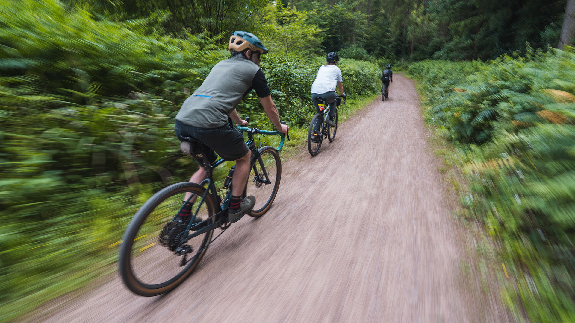 Three riders cycling down a gravel track in the Forest of Dean. Riders shown from the rear.