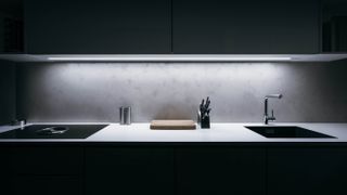 A dark kitchen with overhead counter lights illuminated