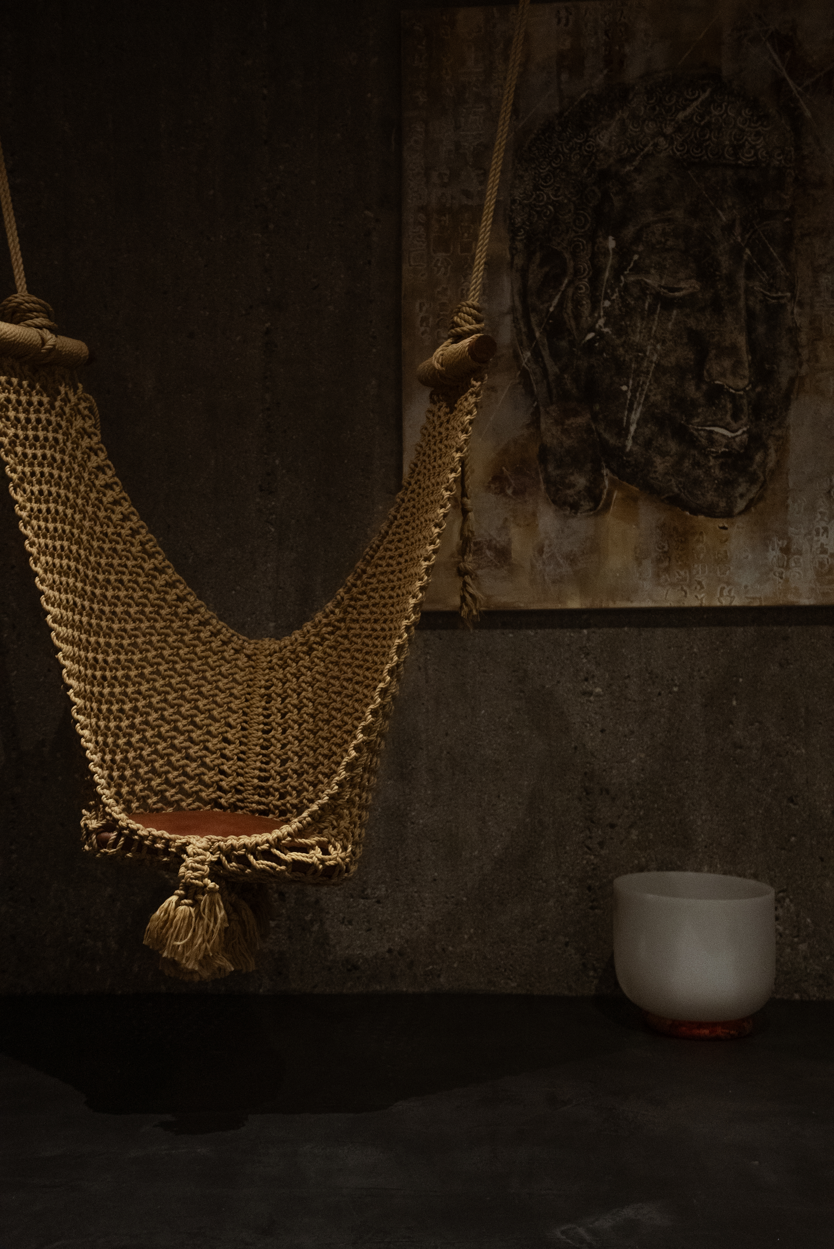 A textile swing placed inside a dimly lit room filled with textural decor and artworks.