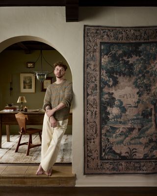 Drew Michael Scott poses alongside a his collection's Hollyhock rug, inspired by antique Verdure tapestries.