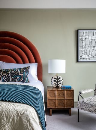 Gray green bedroom with orange headboard and wood nightstand