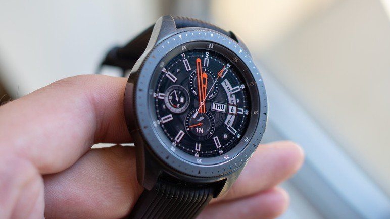 A photo of the Samsung Galaxy Watch (2018) held in someone's hand, showing a Classic-style bezel and watch face.